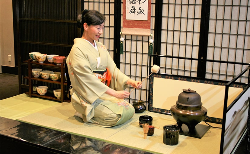 畳ステージの上で茶道を体験する女性の写真