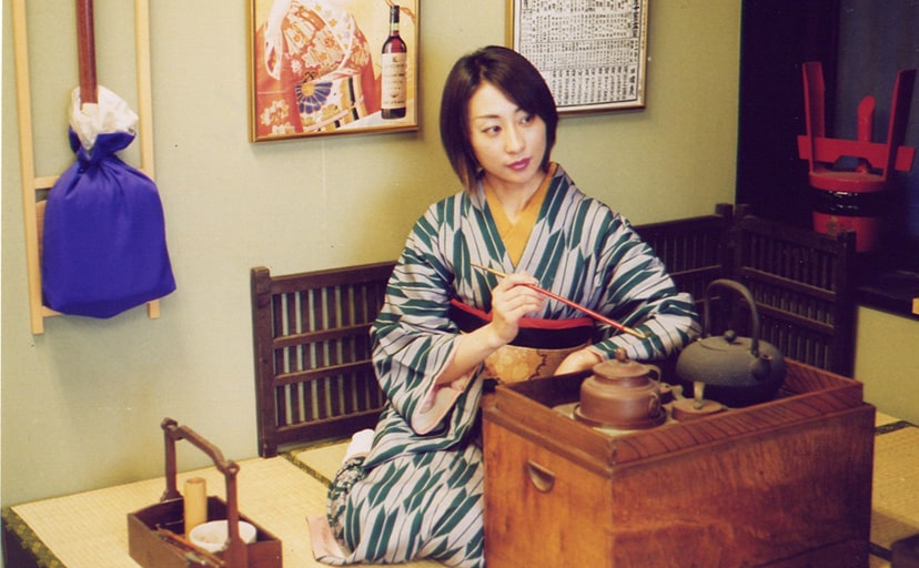 小道具のキセルを手に持ちセットに座る大正風の着物を着た女性の写真
